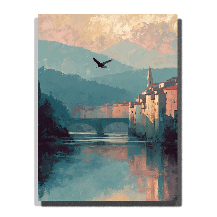 Riverside town with stone bridge, church spire, flying bird, teal mountain layers, warm buildings, and calm water reflections, paint by numbers wall art by PaintEasy