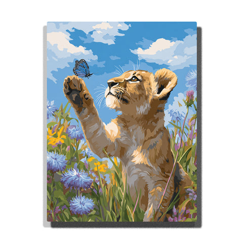 Lion cub reaching for a butterfly in a wildflower meadow with raised paw, golden fur, blue blossoms, yellow flowers, green grass, and bright sky, paint by numbers wall art by PaintEasy
