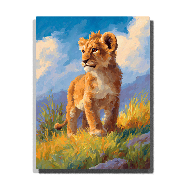 Lion cub standing in sunlit meadow grass with golden-brown fur, cream chest, blue sky, white clouds, and soft grassy hillside, paint by numbers wall art by PaintEasy
