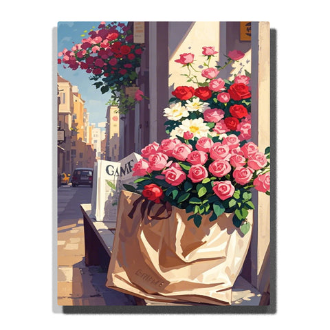 Pink and red roses in a paper bag by a sunlit flower shop window, with a narrow city street and hanging basket in the background in this Paint by Numbers artwork.