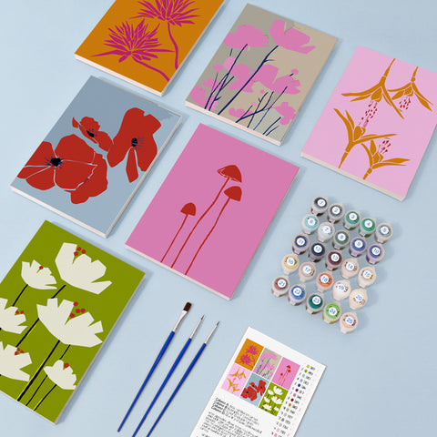 Six mini paint by numbers canvases arranged in a set, each featuring a colorful floral silhouette illustration including poppy flowers, lotus-style blooms, lily shapes, wildflower stems, and abstract botanical designs. Each artwork uses a flat graphic style with bold color blocks, simplified floral outlines, and modern decorative composition.