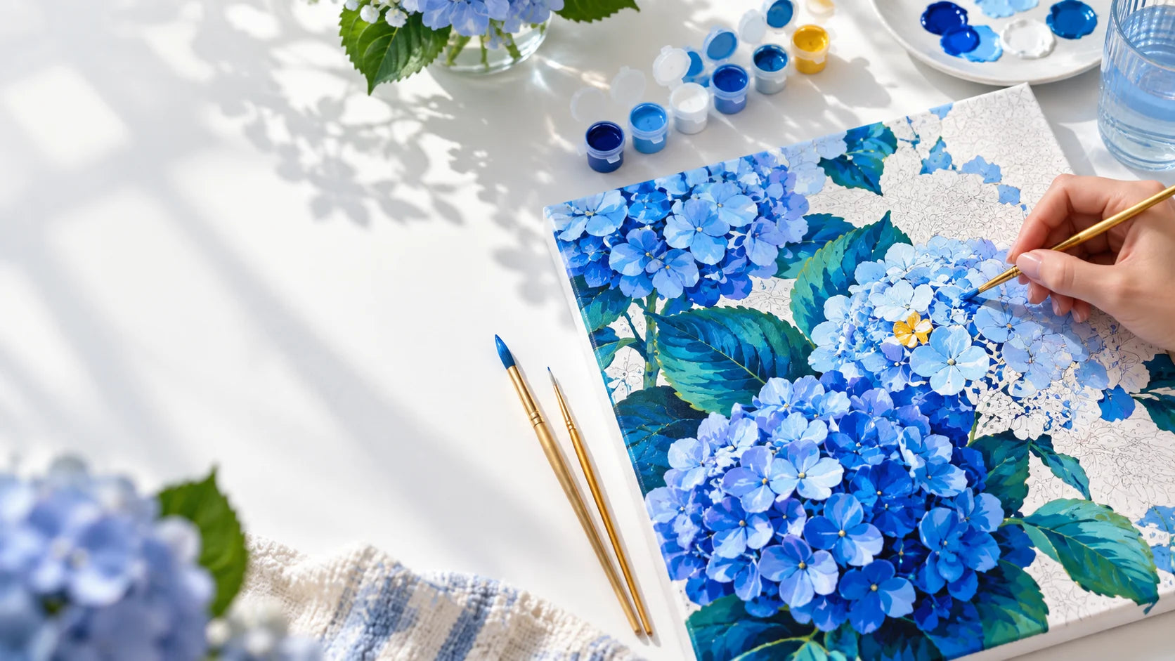 A hand painting blue hydrangeas on a PaintEasy canvas
